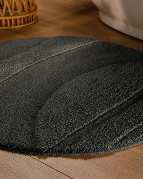 Runder Badteppich mit geschwungenem Linienmuster auf einem Holzboden in einem Badezimmer neben einer Badewanne.