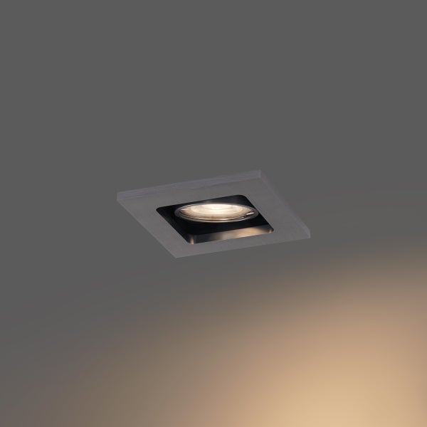 Quadratischer Einbaustrahler aus gebürstetem Metall mit eingeschaltetem Leuchtmittel.