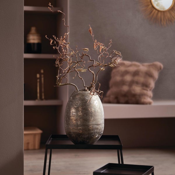 Eiförmige Vase mit antiker Textur und gedrehten Zweigen auf einem schwarzen Metalltisch in einem modern gestalteten Raum.