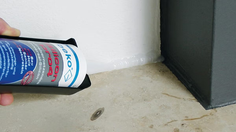 Eine Kartusche beko Silicon pro4 Universal-Silikon wird mit einer Kartuschenpresse aufgetragen, um eine Fuge zwischen Wand und Boden zu versiegeln.