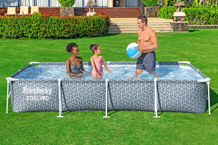 Rechteckiger Bestway Steel Pro Aufstellpool mit Blattmuster und Metallrahmen in einem hellen Garten, eine Familie spielt mit einem Wasserball im Pool.