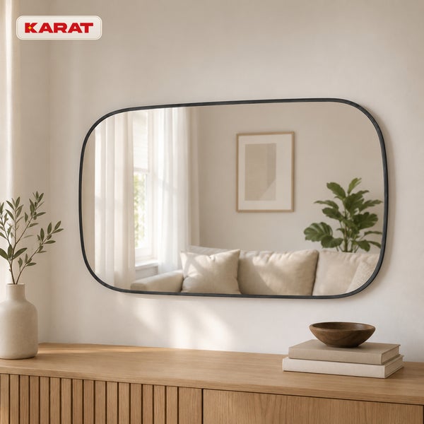 Wandspiegel mit abgerundeten Ecken und Rahmen über einer Holzkommode im Wohnzimmer. Karat Logo.