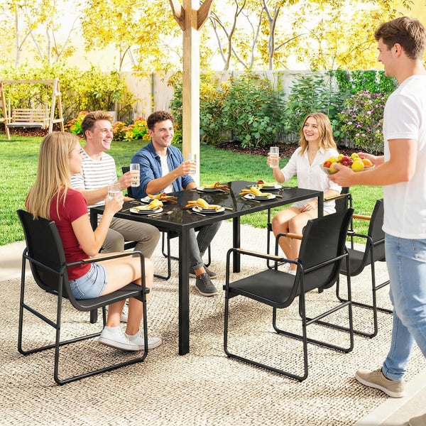 Moderne Garten-Essgruppe mit schwarzem Glastisch und Stühlen in einer sonnigen Gartenanlage mit Personen beim gemeinsamen Essen.