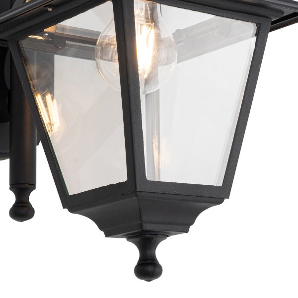 Nahaufnahme einer schwarzen Außenwandleuchte in Laternenform mit Glaseinsätzen und leuchtendem LED-Filament-Leuchtmittel.