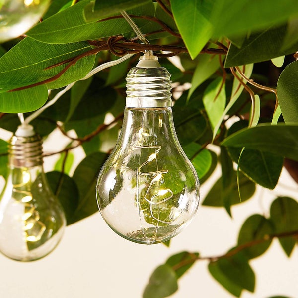 LED-Lichterkette in Glühbirnen-Optik mit feinem Draht und kleinen LEDs im Inneren, aufgehängt an grünen Pflanzenblättern im Garten.