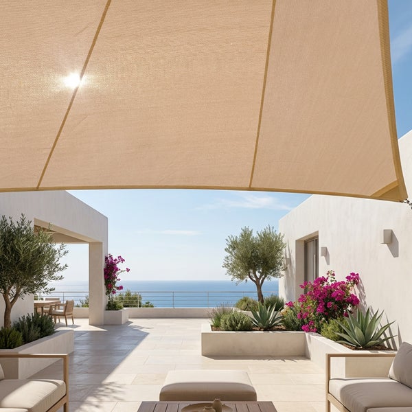 Sonnensegel über einer hellen mediterranen Terrasse mit Meerblick, Gartenmöbeln und Olivenbäumen.