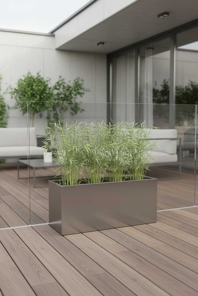 Ein rechteckiger Pflanzkasten aus Metall mit Bambuspflanzen auf einer modernen Holzterrasse mit Glasgeländer und Gartenmöbeln.