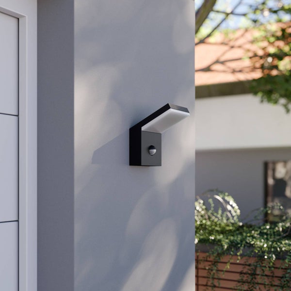 Moderne schwarze Außenwandleuchte mit Bewegungsmelder montiert an einer grauen Hauswand.