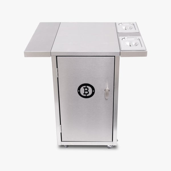 Innenansicht eines Gartenhauses aus Holz mit Sofa, Sessel und Regal sowie Fahrrad und Pflanzen im Außenbereich.