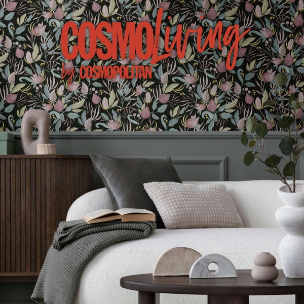 Wohnzimmer mit Vliestapete mit Blumenmuster vor einem hellen Sofa und einem dunklen Holzmöbelstück.