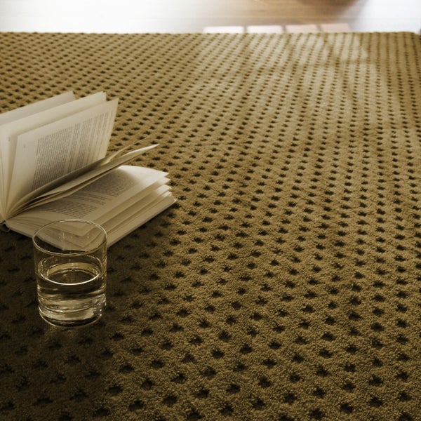Strukturierter Teppichboden mit regelmäßigem Waffelmuster in einer Wohnszene mit Buch und Wasserglas.