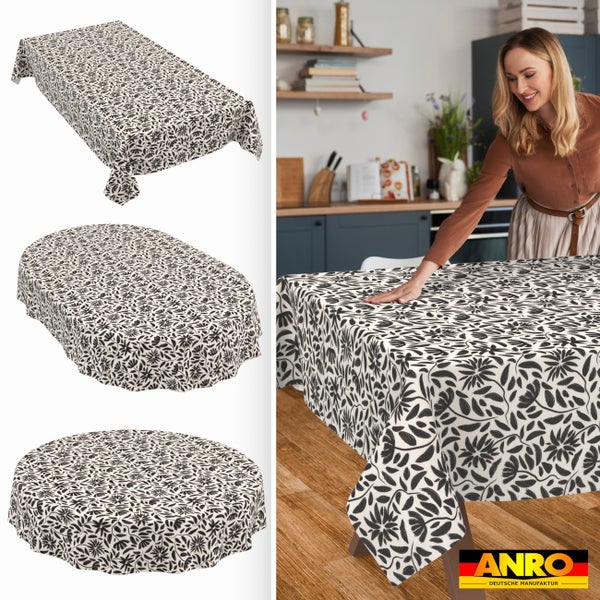 Tischdecke mit floralem Muster in Schwarz-Weiß, rechteckig, oval und rund. Frau an Küchentisch. ANRO DEUTSCHE MANUFAKTUR Logo.
