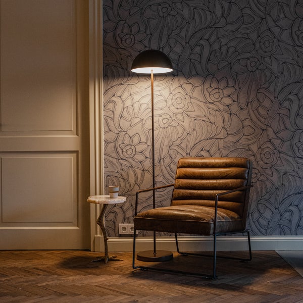 Gut beleuchteter Wohnbereich mit Ledersessel, Stehleuchte, Beistelltisch und gemusterter Tapete auf Fischgrätparkett.