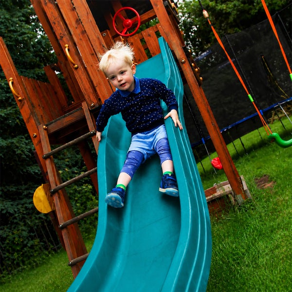 Kind auf einer Wellenrutsche an einem Spielturm aus Holz im Garten.
