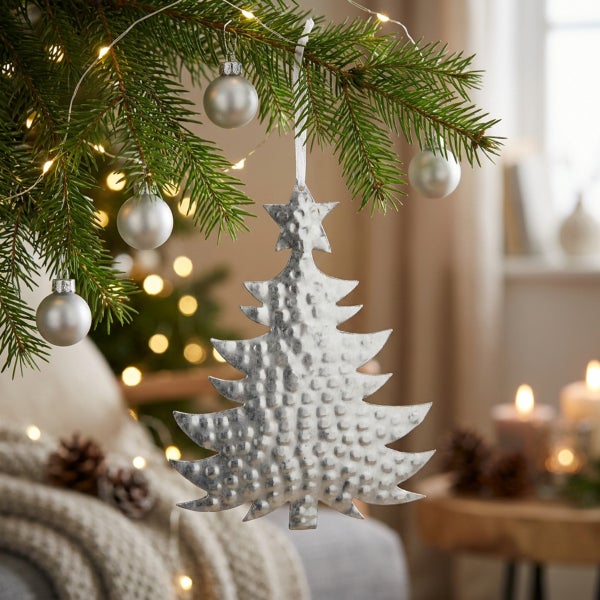 Weihnachtsbaumanhänger in Form eines Tannenbaums mit Hammerschlagoberfläche aus Metall hängend an einem Weihnachtsbaum mit Lichterkette