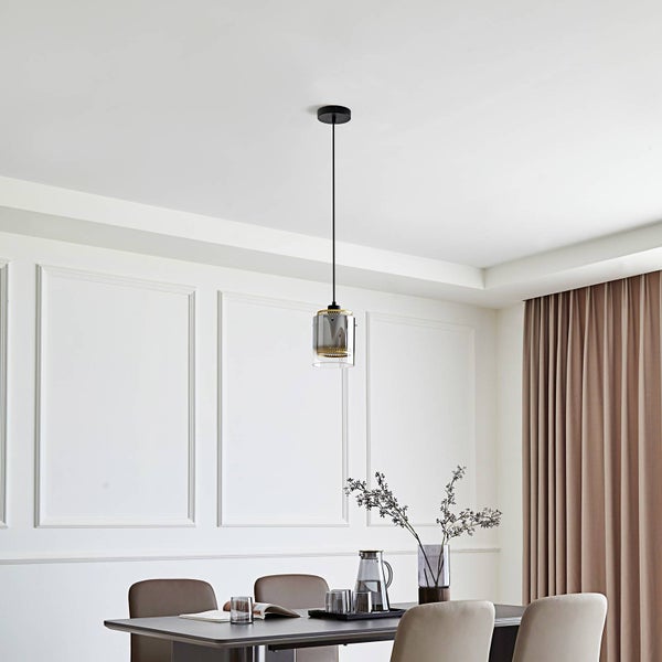 Moderne Pendelleuchte mit zylindrischem Glasschirm über einem Esstisch in einem hellen Esszimmer mit dekorativen Wandleisten.