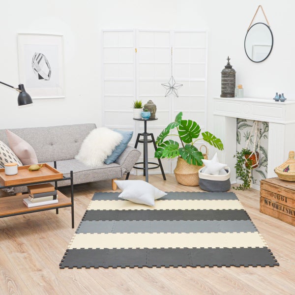 Gestreifte Puzzlematte aus Schaumstoff in einem hellen, modern eingerichteten Wohnzimmer mit grauem Sofa und Holzboden.