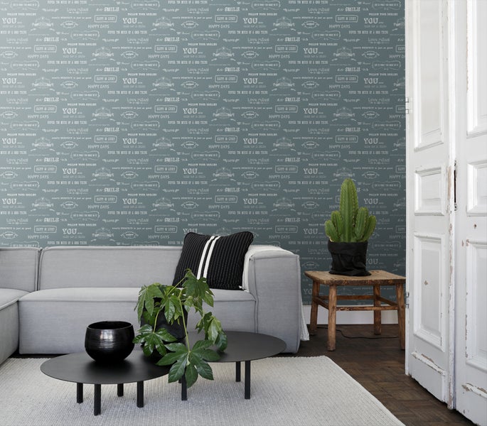 Wohnzimmer mit grauer Couch, Couchtisch und Wandtapete mit Schriftzugmuster