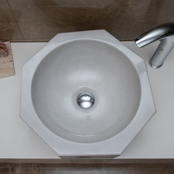 Draufsicht auf ein achteckiges Aufsetzwaschbecken in Naturstein-Optik mit verchromter Armatur auf einem weißen Waschtisch.