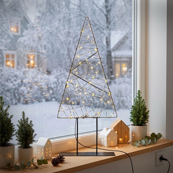 Dekorative Weihnachtsbaum Silhouette aus Metall mit LED Beleuchtung stehend auf einer Fensterbank mit Winterdeko vor einem verschneiten Garten