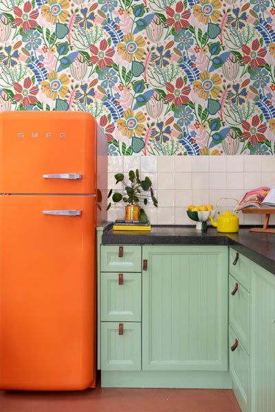 Farbenfrohe Küche mit leuchtend orangem Retro Kühlschrank, mintgrünen Schränken mit Ledergriffen und einer lebhaften Blumentapete.