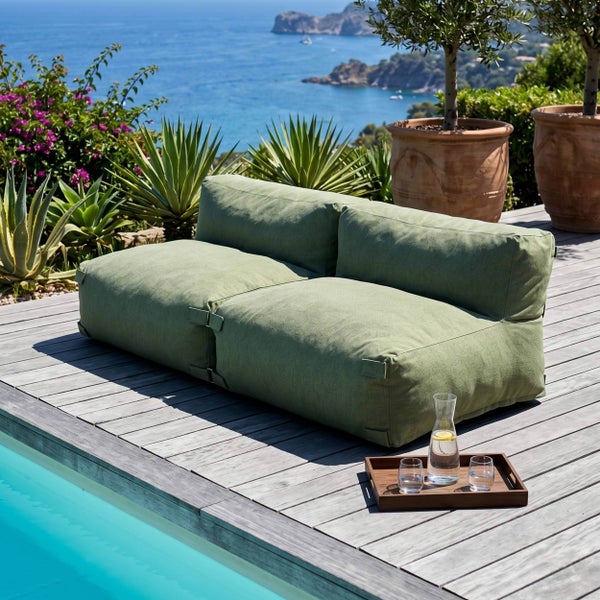 Grünes Zweisitzer Outdoor Lounge Sofa auf einer Holzterrasse am Pool mit Meerblick und mediterranen Pflanzen.