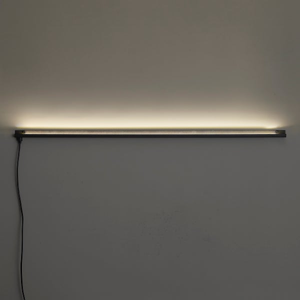 Schlanke horizontale LED-Lichtleiste an einer Wand montiert mit nach oben gerichtetem warmweißem Licht und sichtbarem Stromkabel.