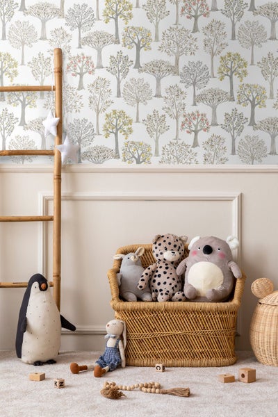 Vliestapete mit Baumuster in einem hellen Kinderzimmer mit Rattansessel, Stofftieren, Holzwürfeln und einer Bambusleiter.