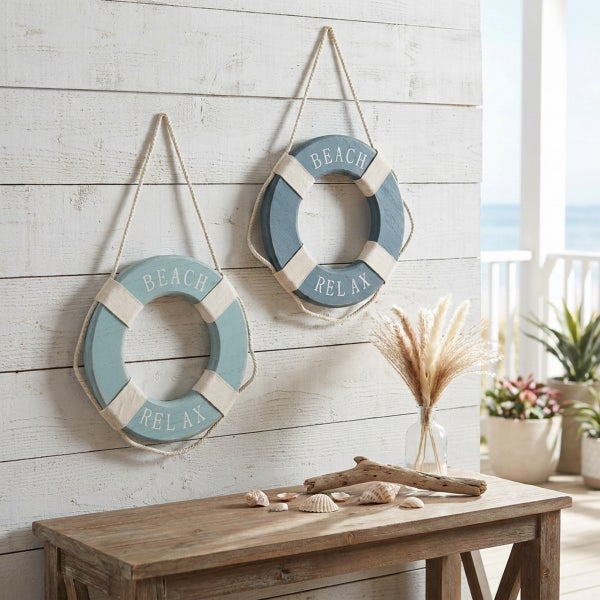 Zwei maritime Rettungsringe als Wanddekoration mit Beach Relax Aufschrift über einem Holztisch mit Dekoration im Strandhaus Stil.