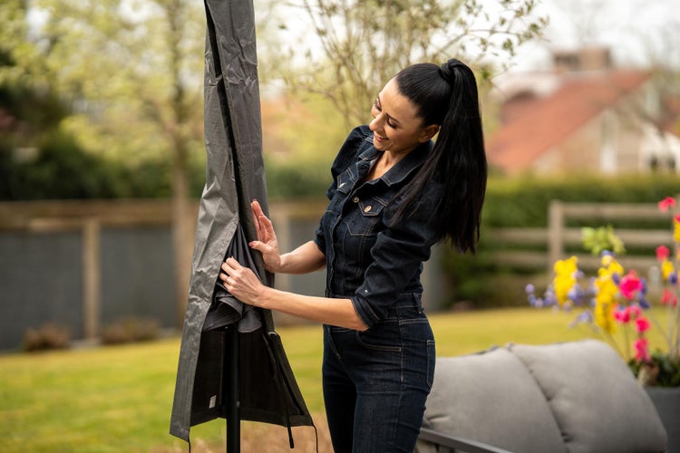 Eine Frau zieht eine Schutzhülle über einen Gartenschirm im Freien.