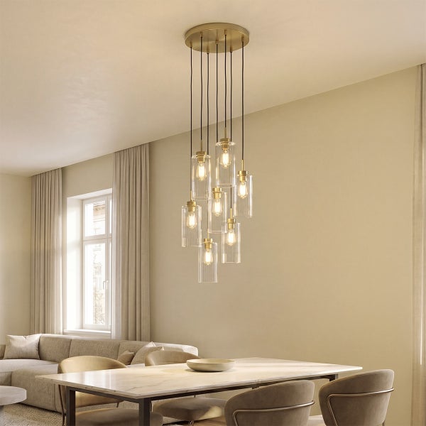 Moderne Pendelleuchte mit neun zylindrischen Glasleuchten an einer Deckenhalterung über einem Esstisch in einem hellen Wohnzimmer.