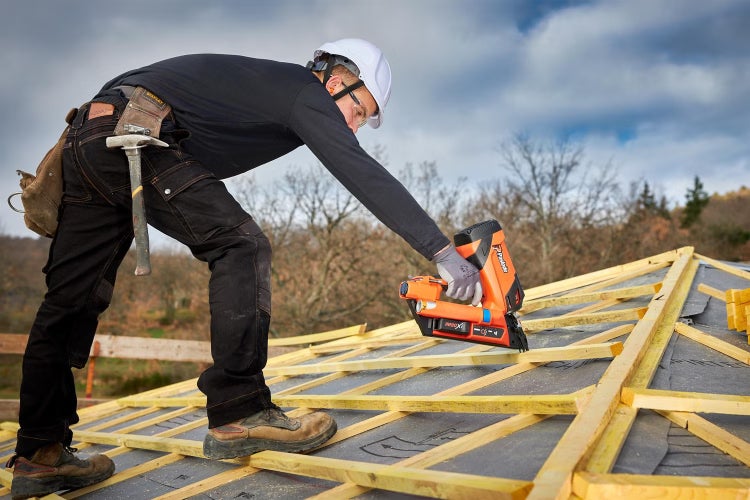 Handwerker mit Schutzhelm arbeitet auf einem Dachgerüst mit einem Paslode gasbetriebenen Nagelgerät bei der Holzkonstruktion