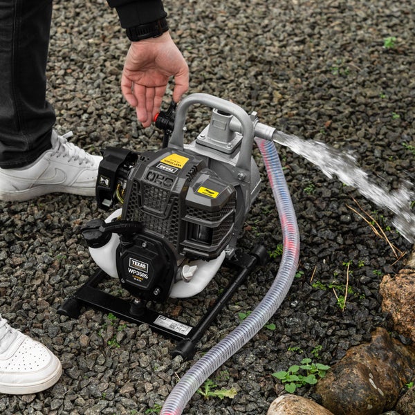 Eine handbediente Texas WP358S Benzin Wasserpumpe mit Vier Takt Motor beim Pumpvorgang auf kiesigem Untergrund.