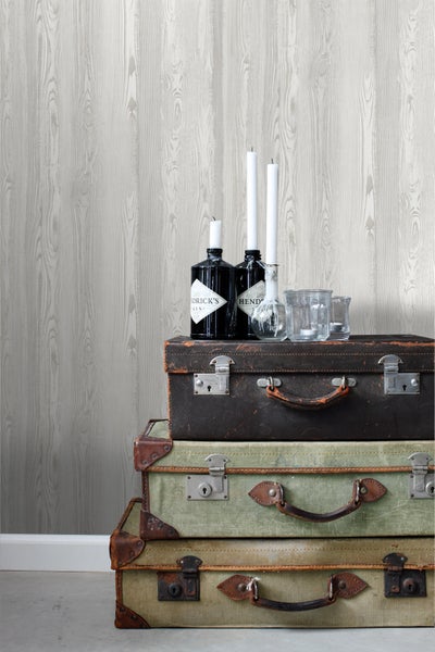 Dekorative Szene mit Kofferstapel, Getränkeflaschen und Kerzen vor einer Tapete mit Holzmaserung.