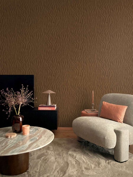 Wohnzimmer mit Vliestapete mit wellenförmigem Textilmuster in einer modernen, gemütlichen Einrichtung mit Sessel und Beistelltisch.