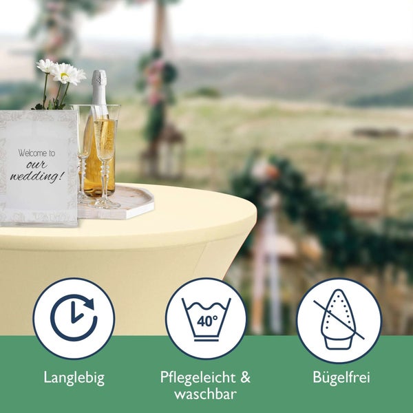 Szene mit Stretchhusse auf einem Tisch im Freien, dekoriert mit Blumen, Sekt und einem Schild mit der Aufschrift "Willkommen zu unserer Hochzeit!". Waschbar bei 40 Grad. Bügelfrei und langlebig.