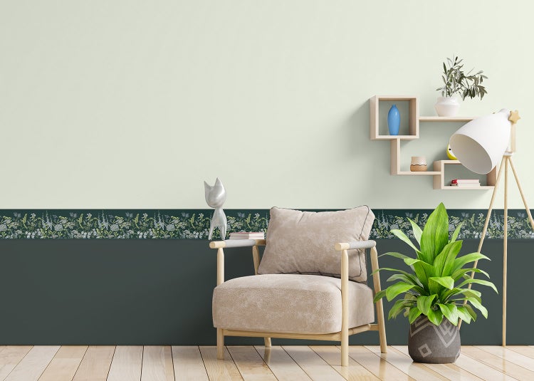 Wohnzimmer mit floraler Wandbordüre, Sessel, Zimmerpflanze, Stehlampe auf Holzstativ und Wandregal auf hellem Holzfußboden.