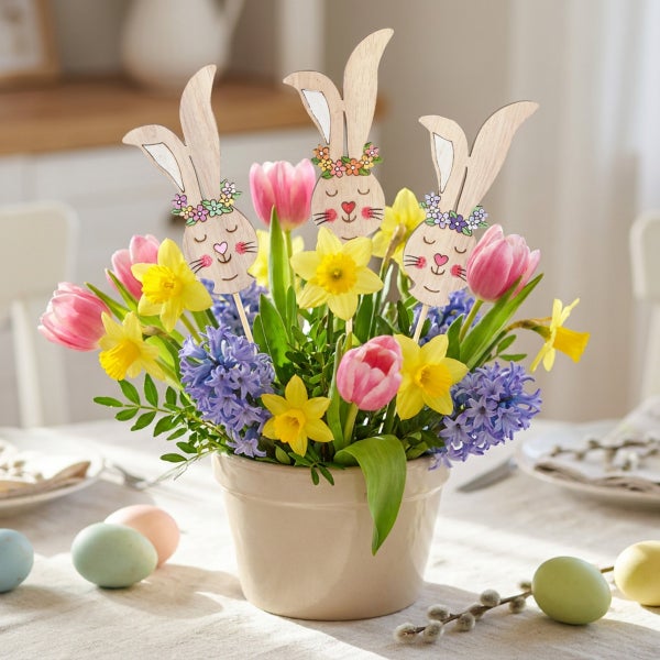 Ostergesteck im Topf mit drei Holzhasen Steckern, Tulpen, Narzissen und Hyazinthen als frühlingshafte Tischdekoration für Ostern.