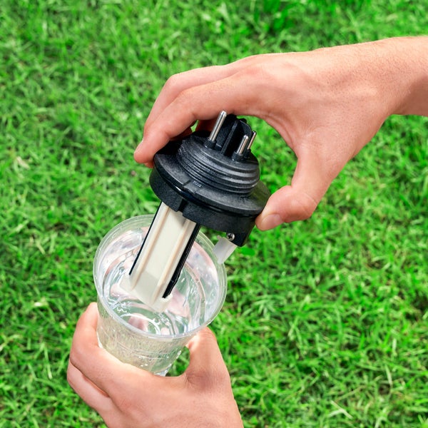 Eine Person taucht einen Feuchtigkeitssensor in ein Glas Wasser.