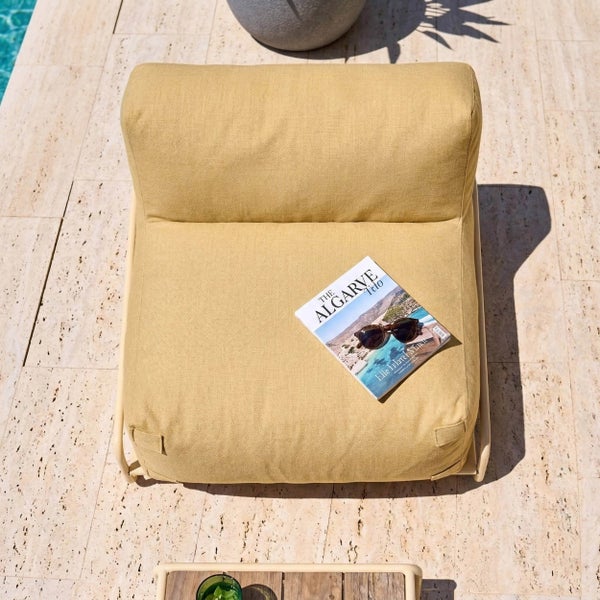Gelber Outdoor-Lounge-Sessel auf einer Terrasse aus Naturstein neben einem Pool, Ansicht von oben mit Magazin und Sonnenbrille.
