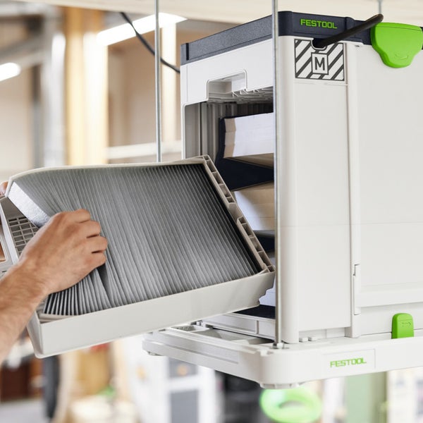 Ein gefalteter Ersatzfilter wird in ein Festool Luftreinigungsgerät mit Festool Logo und Staubklasse M Kennzeichnung eingesetzt.