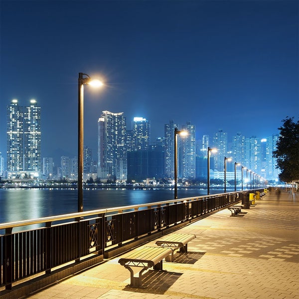 Nachtaufnahme einer Uferpromenade mit Stadtbild, Laternen und Sitzbänken