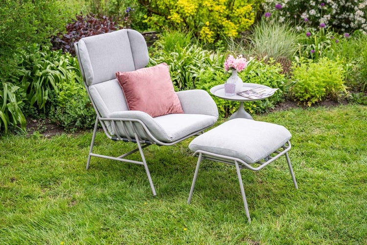 Moderner Garten-Loungesessel mit hoher Rückenlehne, passendem Hocker und Beistelltisch in einer grünen Gartenumgebung.