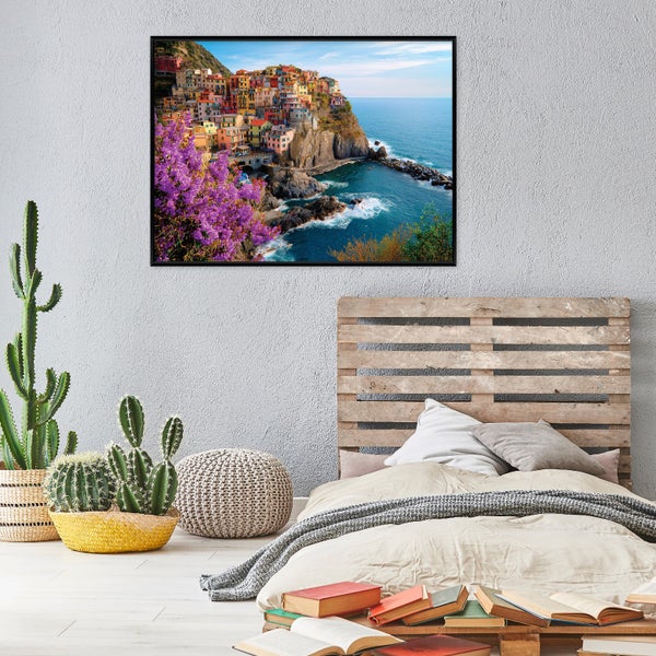 Modern eingerichtetes Schlafzimmer mit Palettenbett, Kakteen und einem Wandbild eines italienischen Küstendorfes an einer grauen Wand.