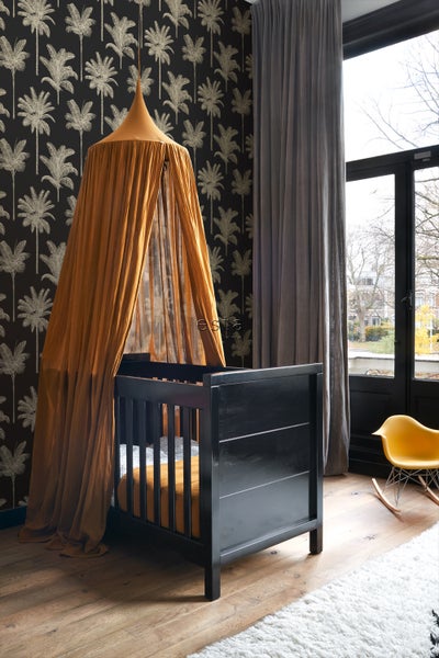 Kinderzimmer mit schwarzem Gitterbett und Baldachin vor einer Palmentapete