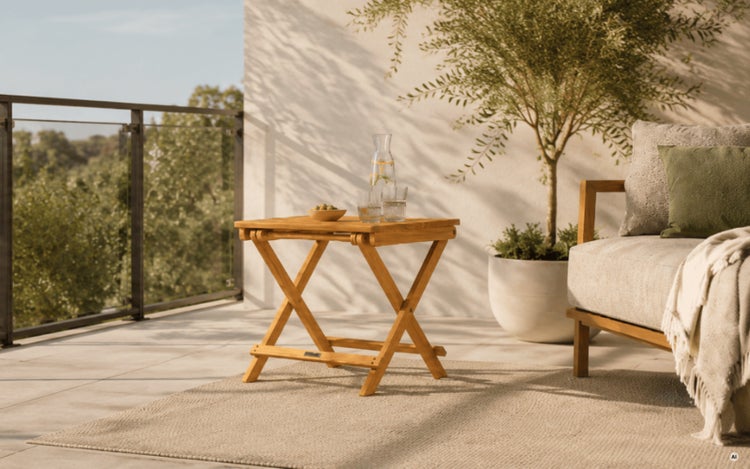Quadratischer Klapptisch aus Holz auf einer Terrasse mit Glasgeländer, Sofa und Olivenbaum im Hintergrund.