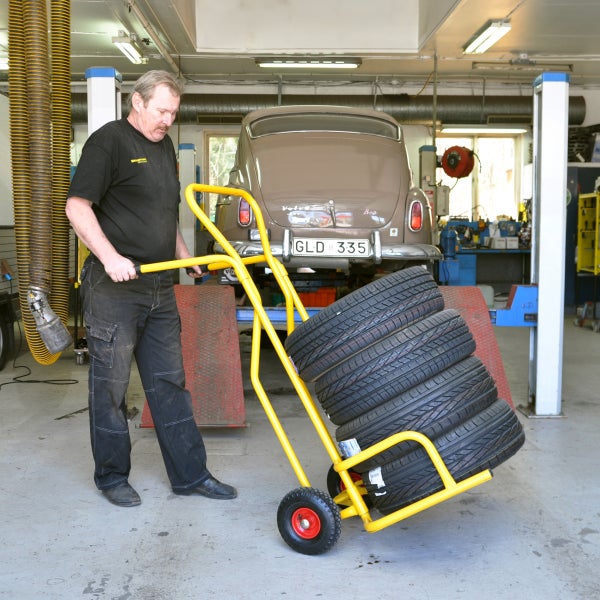 Ein Mann schiebt einen gelben Transportwagen mit Reifen in einer Werkstatt.