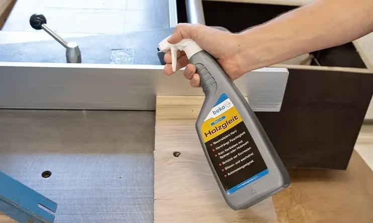 Eine Hand hält eine Sprühflasche Beko Holzgleit zur Anwendung auf einer Holzbearbeitungsmaschine.
