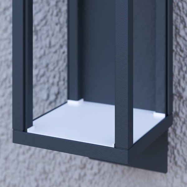Nahaufnahme einer modernen Außenwandleuchte mit dunklem Metallrahmen und weißem Diffusor an einer strukturierten Hauswand.