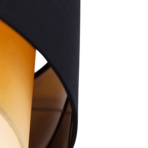 Nahaufnahme eines modernen Lampenschirms mit geschwungenen, überlappenden Elementen aus Stoff und Metall in Schwarz und Gold.